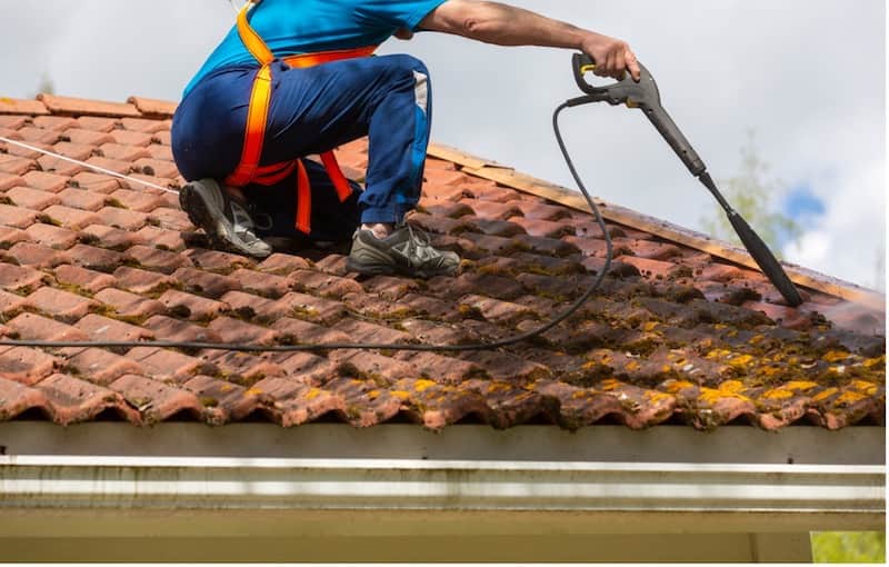 Using pressure washer to clean the roof and clear gutters